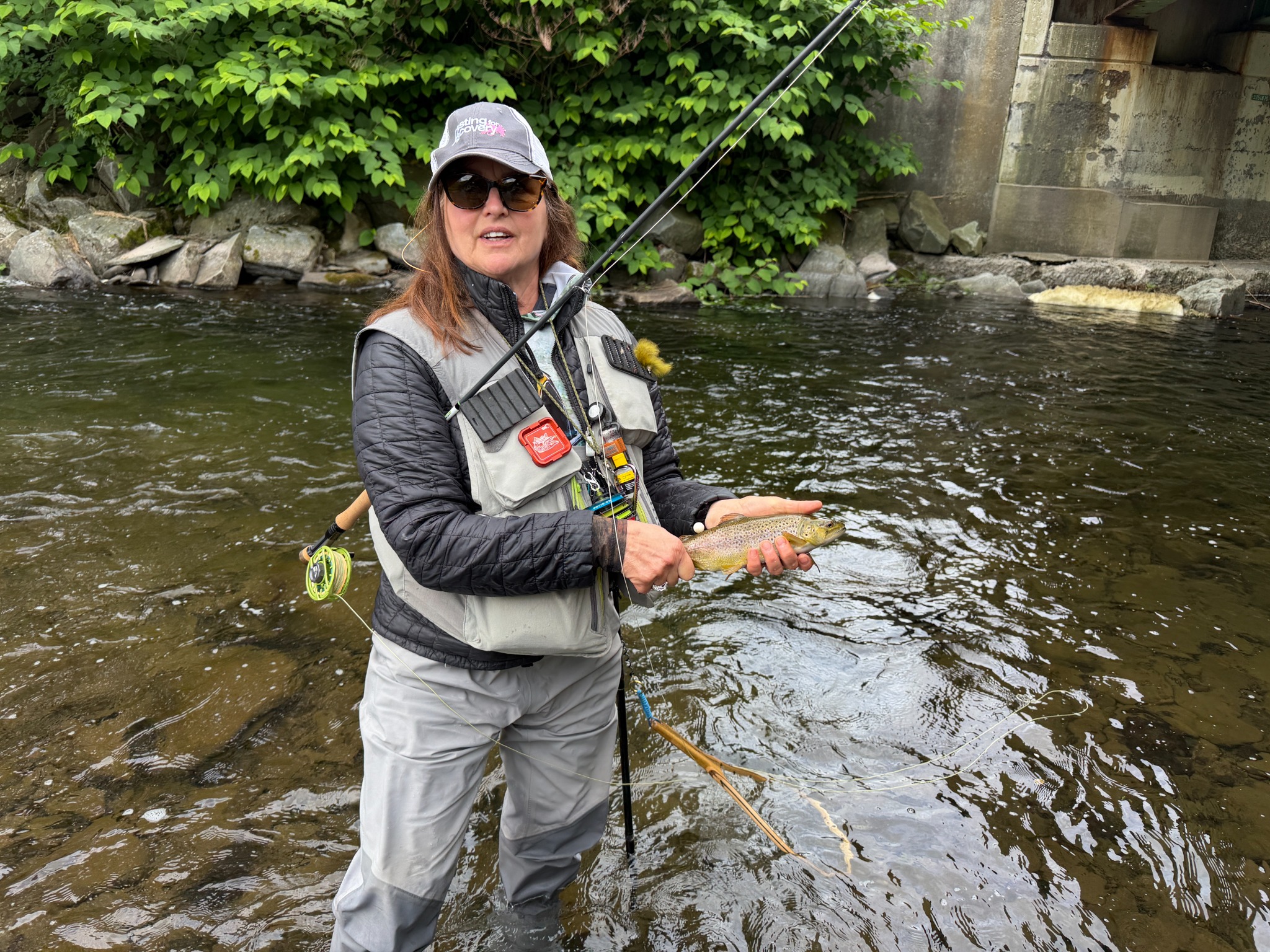 Jill holding a trout while wading a river